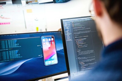 Man from behind in front of two screens with programming code on them