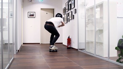 In einem Büroflur fährt ein Mann auf einem Skateboard weg vom Betrachter weg