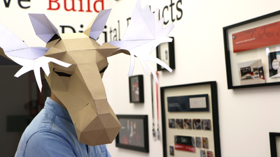 Bürowand mit Bildern und ein Mann in Hemd mit einem Papp-Elch auf dem Kopf