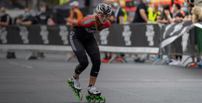 Inlineskaterin auf Rennstrecke mit Publikum hinter der Absperrung