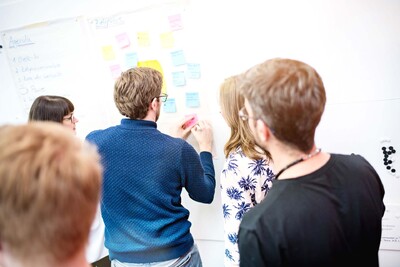 Five people stand in front of a whiteboard with post-its and one of them writes something